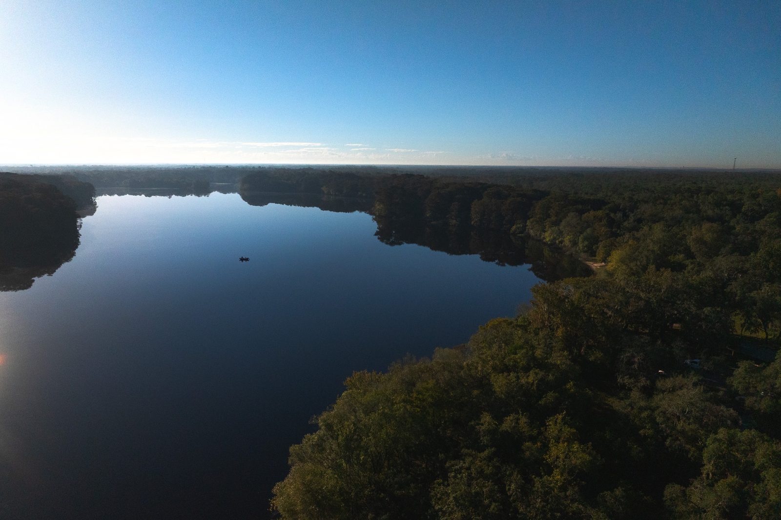 Still lake at dawn from the air, a lone boat and dark treeline