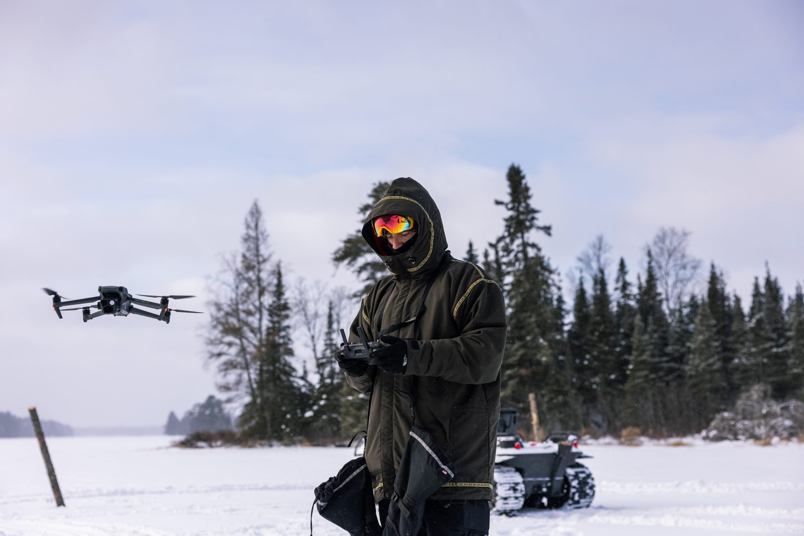 Cameron Melcher in a hooded parka and mirrored goggles flying a drone over a frozen lake