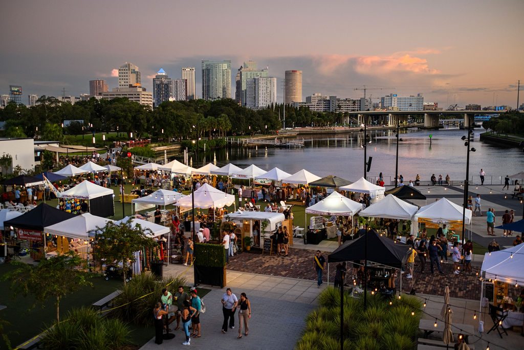 Aerial view of market tents at Armature Works with the Tampa skyline at dusk