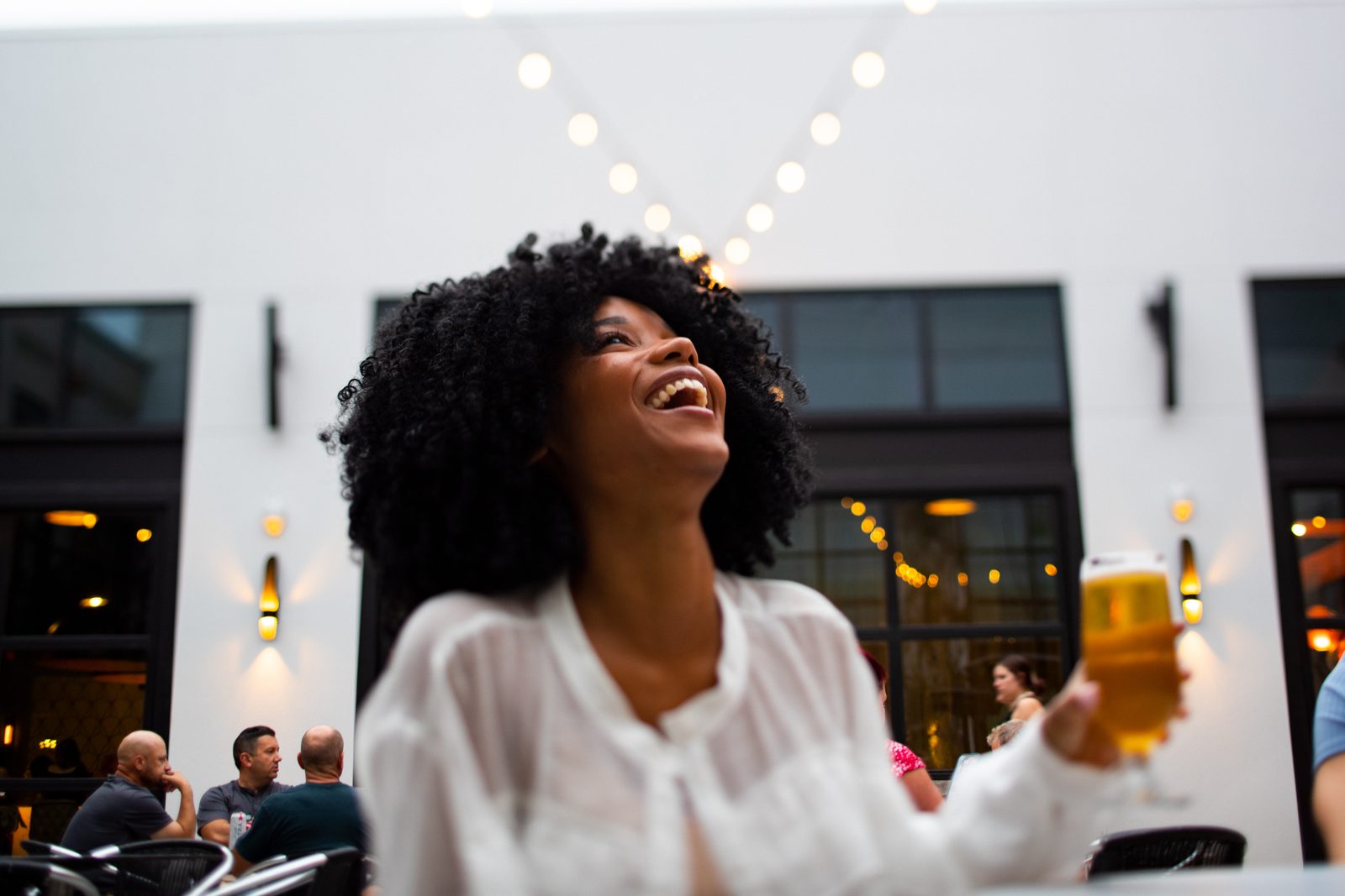 Woman laughing with a beer in hand on a string-lit patio in Tampa