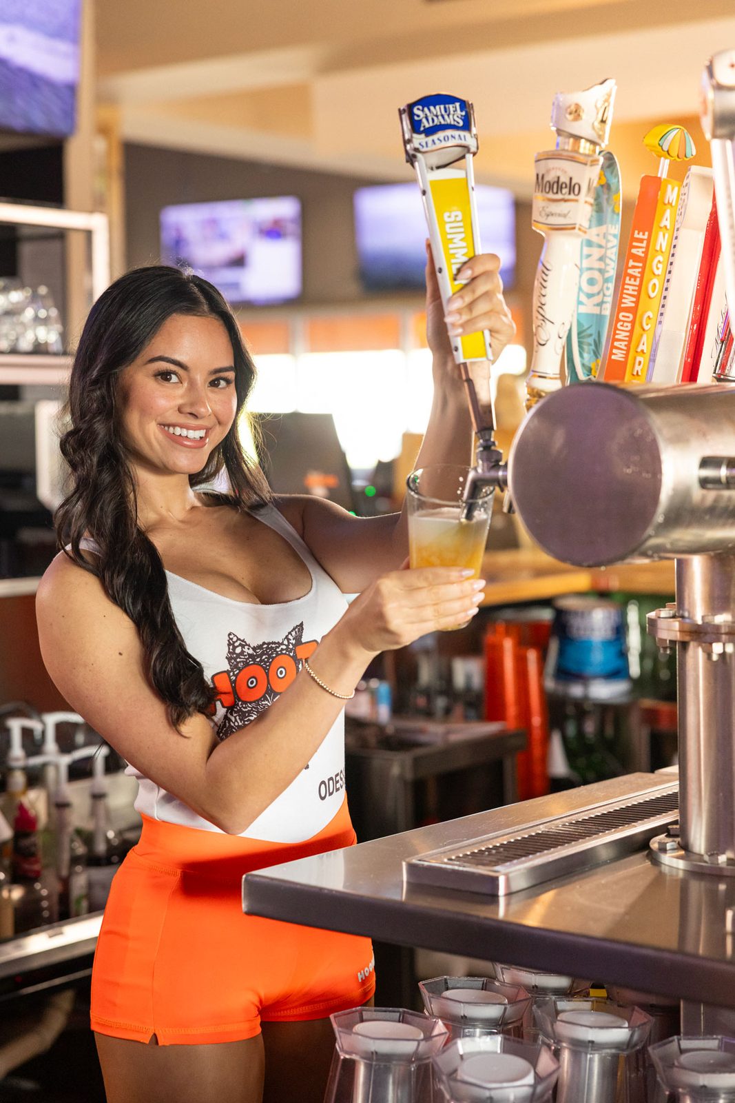Hooters Girl smiling as she pours a draft beer at the bar taps