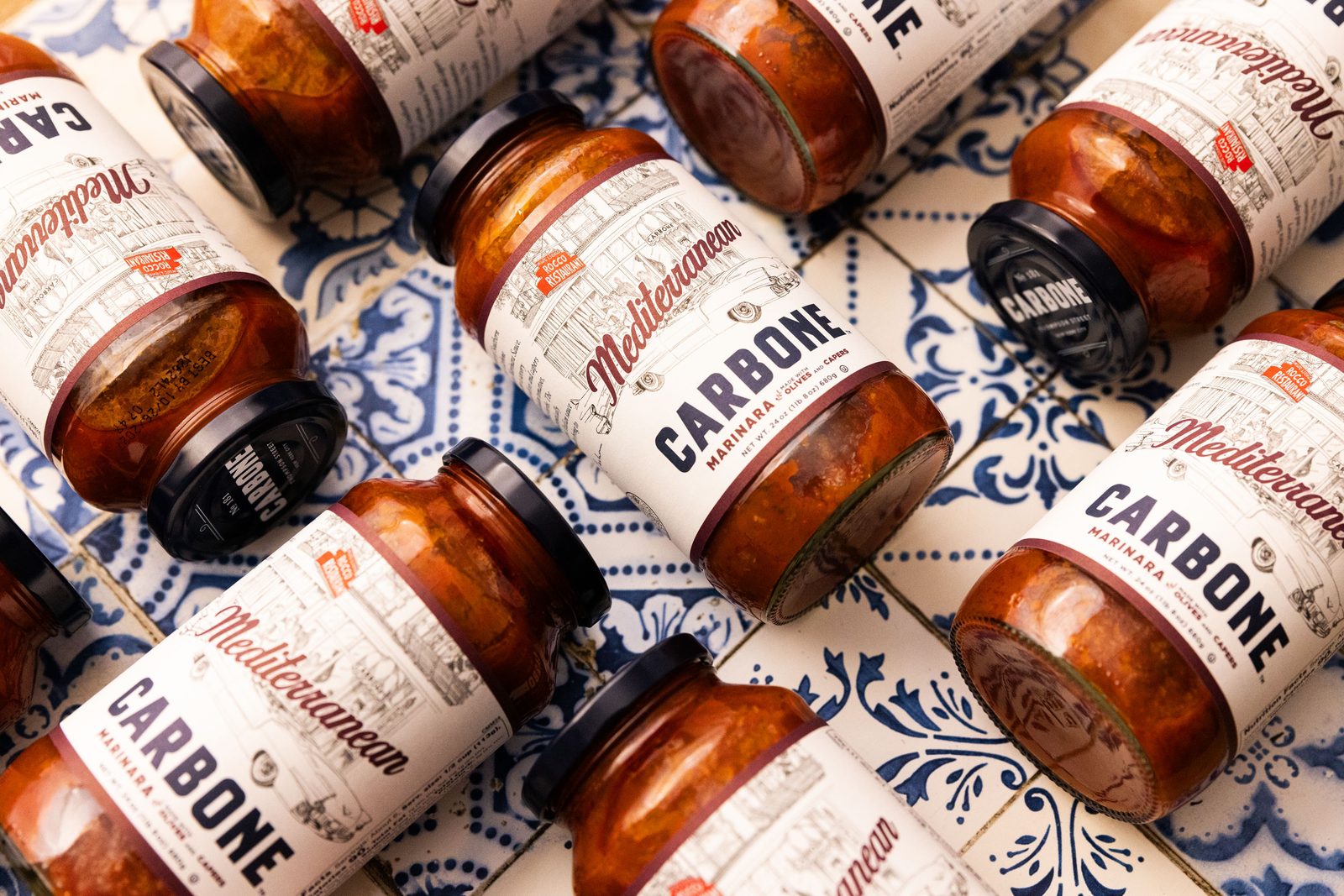 Jars of Carbone marinara sauce arranged on blue and white tile, shot from above