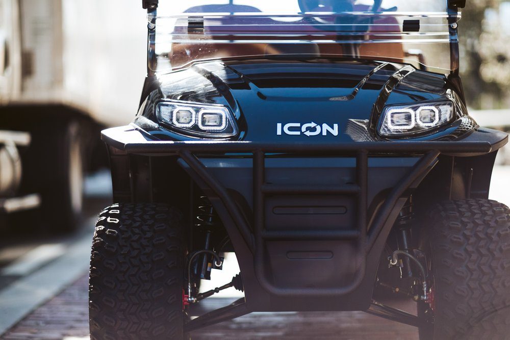 Front of a black ICON electric golf cart with its headlights on, low angle